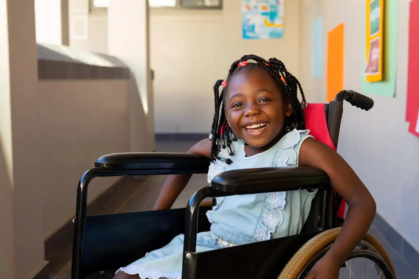 Young girl in a wheelchair smiling in a school hallway