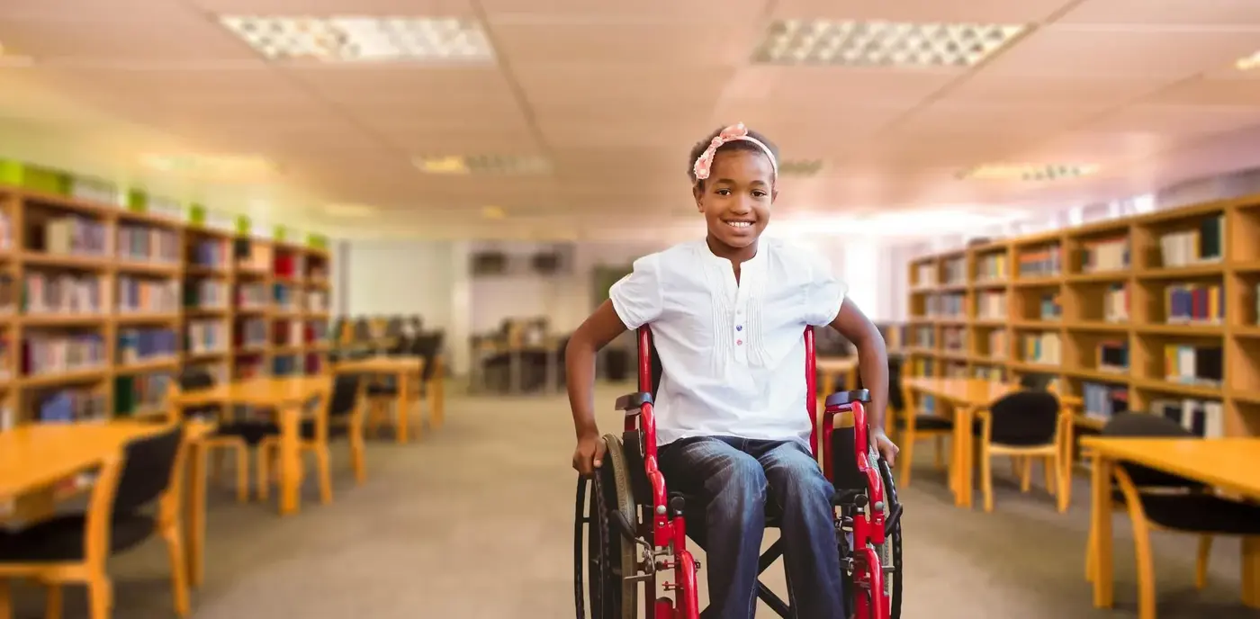 Girl in a red wheelchair smiling in a library