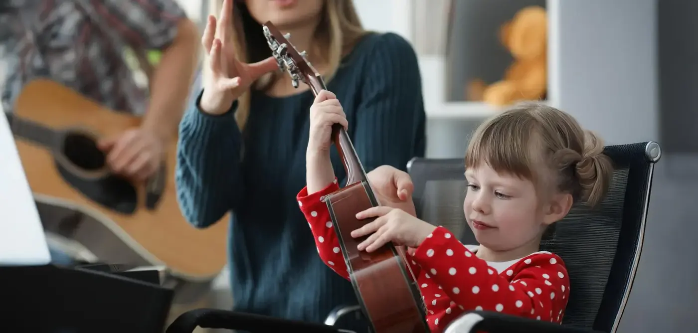 Young child holding a ukulele with an adult helping